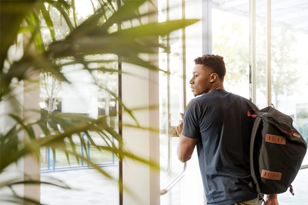 canva-man-looking-outside-window-carrying-black-and-brown-backpack-while-holding-his-hand-on-window-MADGvxKpZew_2024