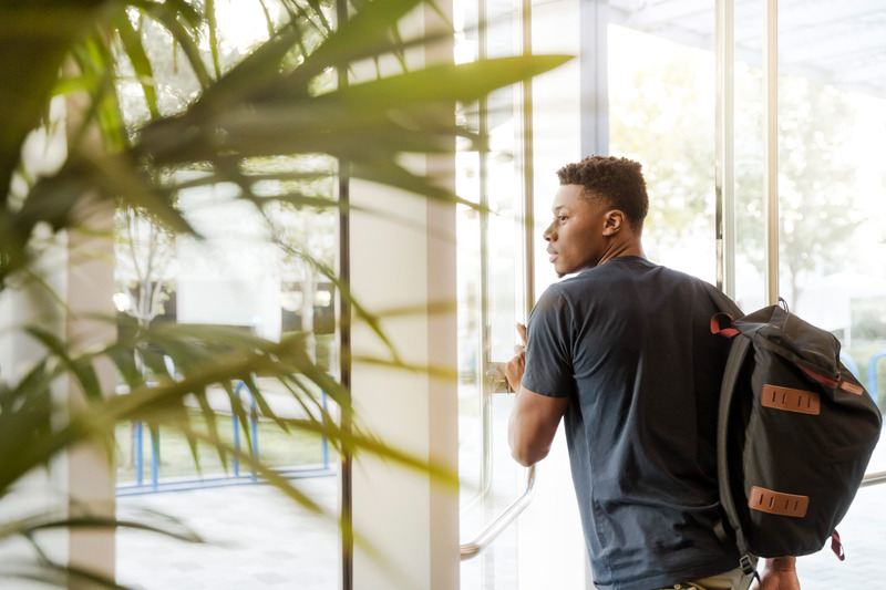 canva-man-looking-outside-window-carrying-black-and-brown-backpack-while-holding-his-hand-on-window-MADGvxKpZew